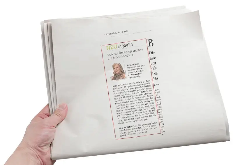 Eine Person hält eine Zeitung hoch, auf der der Name „Brita Richter“ steht.