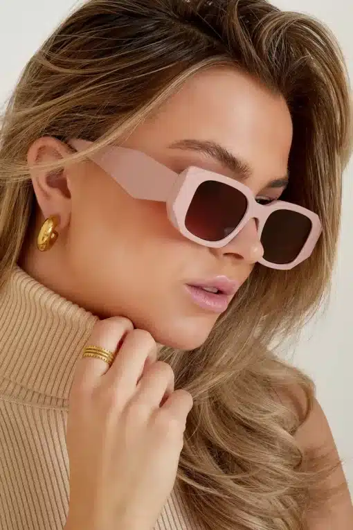 Das Model trägt einen beigen Rollkragenpullover von Trend Sonnenbrille und eine rosa Sonnenbrille.