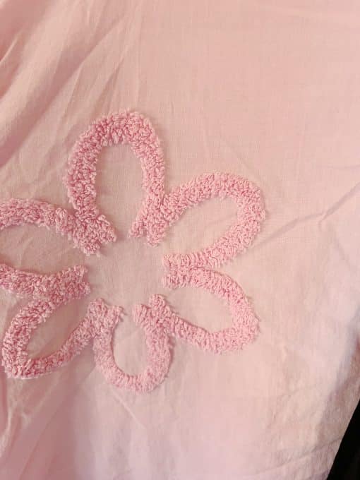 Eine rosa Decke mit einem aufgestickten Blumenhemd.