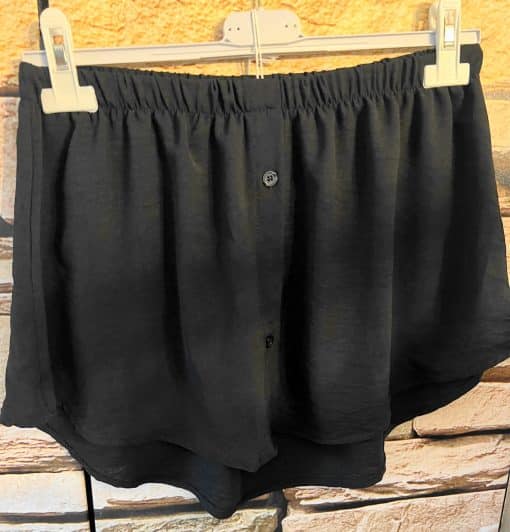 Eine schwarze Shorts hängt an einem Blusentäuscher-Kleiderbügel.