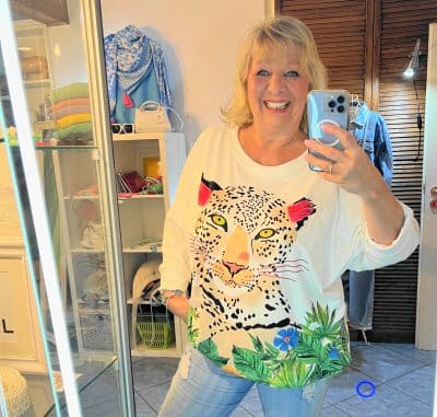 Eine glückliche Frau macht ein Selfie vor einem Spiegel und trägt dabei ein Happy-Leo-Shirt.