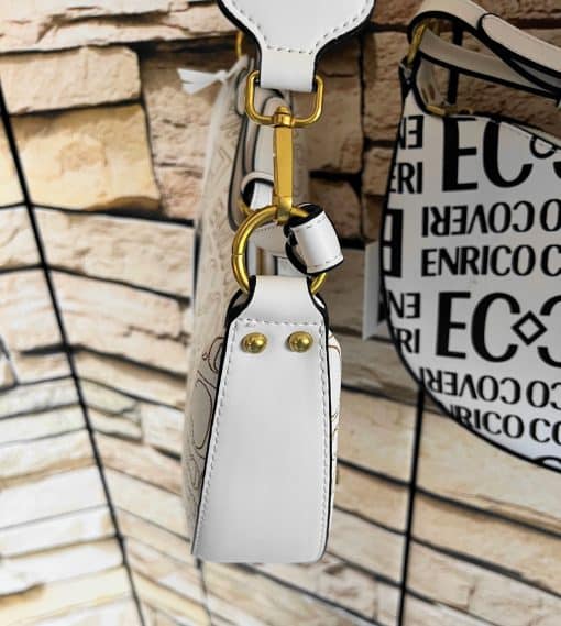 Enrico Tasche: Eine weiße Enrico Tasche Handtasche, die an einer Ziegelwand hängt.