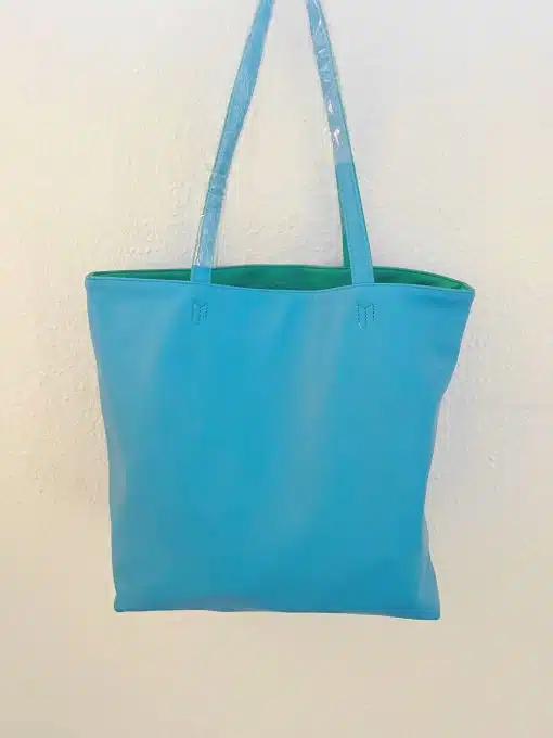 Eine blaue Shopper-Tasche hängt an einer weißen Wand.