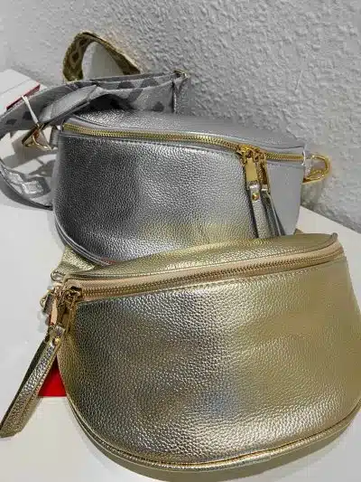 Zwei Cross Body Metallic-Taschen, eine silberne und eine goldene, liegen auf einem Tisch.