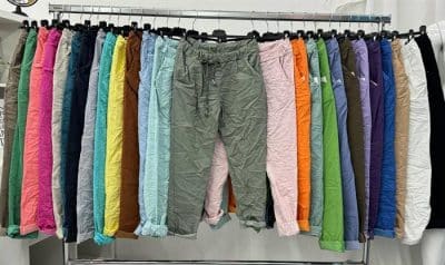 Eine Auswahl bunter Hosen hängt an einem Ständer in einem Geschäft, wobei der Schwerpunkt auf mehreren Farbtönen liegt, darunter Rosa, Blau, Grün und Orange. Willkommen bei unserer neuen Welcome Uni zauberhafte Hose-Kollektion.