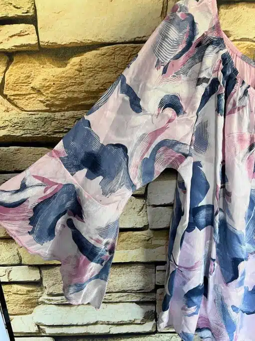 Eine farbenfrohe Graffic-Tunika-Bluse mit abstraktem Design, die an einer Ziegelwand hängt.