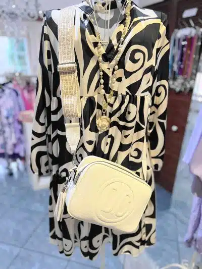 Ein schwarz-weiß gemustertes Kleid auf einem Kleiderbügel, gepaart mit einem weißen DC-Rucksack und einer goldenen Halskette.