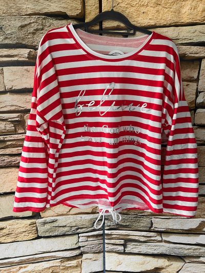 Believe-Shirt (Kopie): Rot-weiß gestreiftes Believe-Langarmshirt mit Textmotiv, das an einer Steinmauer hängt.