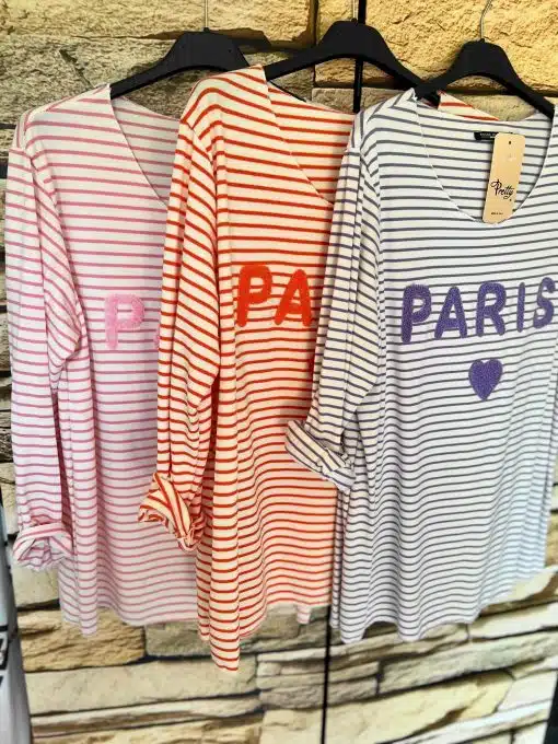 Drei Paris-Streifenhemden mit thematischen Aufdrucken hängen an einem Regal.