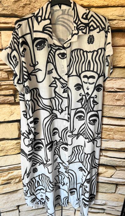 Ein Hemd mit einem abstrakten schwarz-weißen Gesichtsmuster, das an einer Steinmauer hängt, verwandelt sich in Heards Tunika Kleid (Kopie) mit demselben Muster, das jetzt sanft vor demselben Hintergrund schwingt.