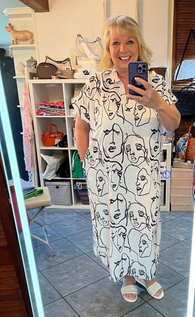 Frau macht ein Spiegel-Selfie und trägt ein Face Tunika-Kleid mit Gesichtsmuster.