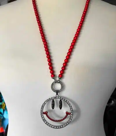 Halskette aus roten Perlen mit einem Lebensbaum-Strass-Wechselanhänger mit Smiley-Detail auf einer Schaufensterpuppe.