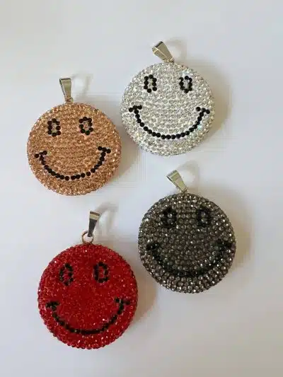 Vier glitzernde Smiley-Schlüsselanhänger mit Big Smile-Wechselanhängern in verschiedenen Farben auf weißem Hintergrund.