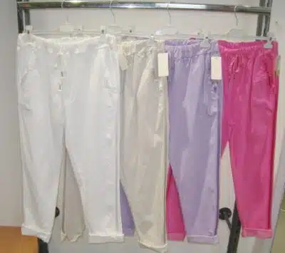 Vier Paar zauberhafte Hosen von By Side hängen an einem Ständer, präsentiert in einem Farbverlauf von Weiß und Beige bis hin zu Hellviolett und leuchtendem Pink, jeweils mit einem sichtbaren Preisschild.