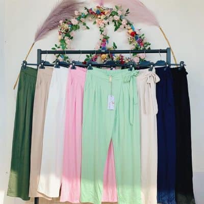Korrigierter Satz: Eine Auswahl bunter Leggings, präsentiert auf einem Kleiderständer, gekrönt von einem dekorativen Blumenbogen und Federn.