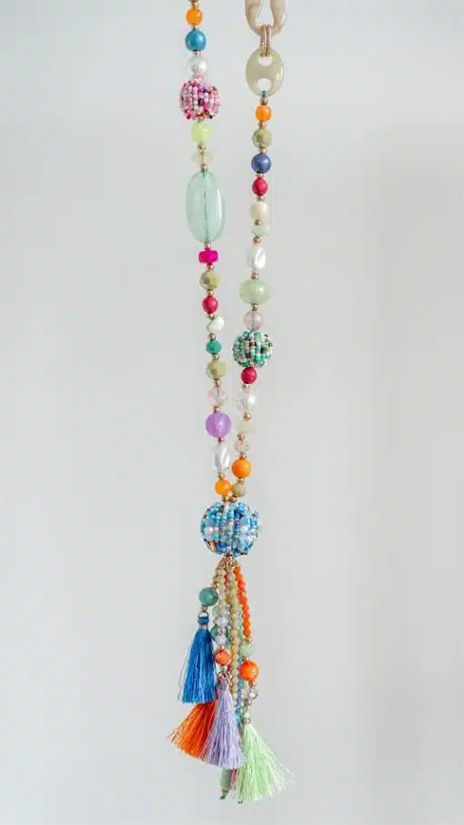 Eine farbenfrohe ball-Boho-Kette (Kopie) mit Perlen in verschiedenen Formen und Größen und Quasten an der Unterseite hängt vor einem weißen Hintergrund.