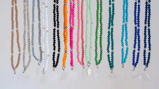 Eine Sammlung bunter Handyketten aus Perlen, die in einer Reihe vor einem weißen Hintergrund präsentiert werden und jeweils einen Kristallanhänger besitzen.