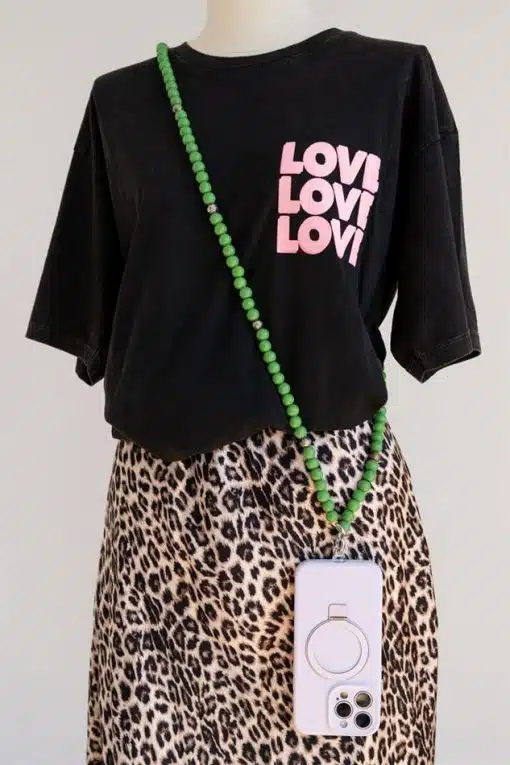 Eine Schaufensterpuppe trägt ein schwarzes T-Shirt mit dreimaligem Aufdruck „Love“ in Pink, dazu einen Rock mit Leopardenmuster. Eine Halskette aus grünen Perlen und ein weißes Smartphone mit einer Handykette.