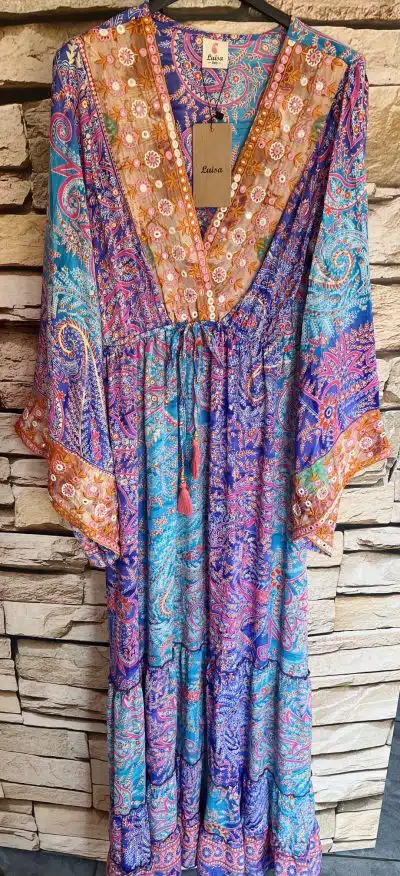 Ein farbenfrohes Indian Summer Boho-Kleid mit Paisley-Muster, das an einer Steinwand hängt.