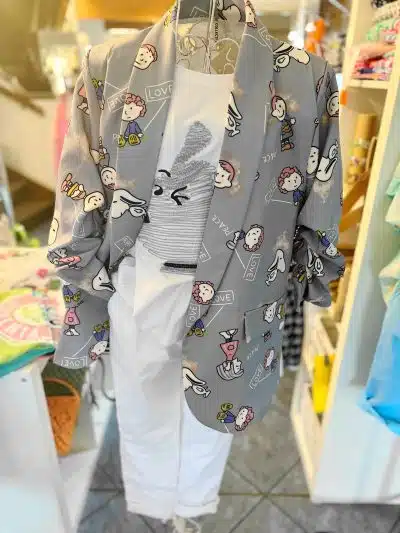In einem Geschäft hängt ein Penauts-Blazer mit Peanuts-Cartoon-Motiven. Der linke Ärmel bedeckt ein weißes Top oder Kleid darunter.