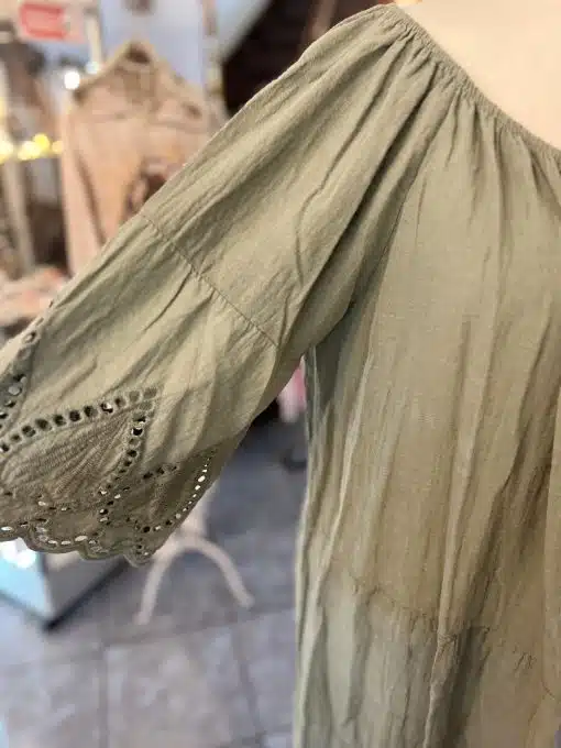 Eine Nahaufnahme eines salbeigrünen Boho-Kleids XL uni mit detaillierter Stickerei und ausgeschnittenen Mustern entlang des Ärmels, präsentiert auf einer Schaufensterpuppe.