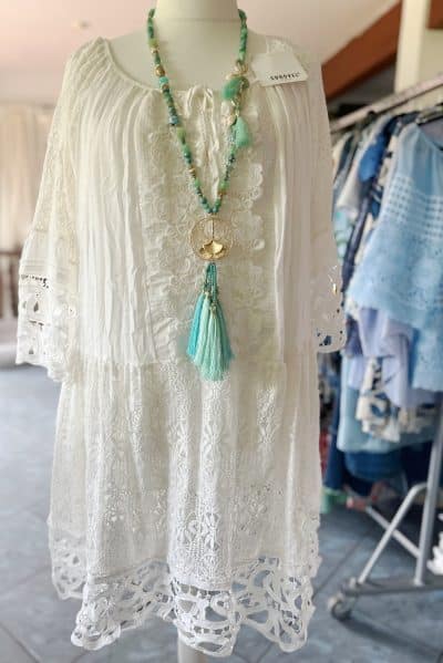 Sunovel Boho Kleid XL wird auf einer Schaufensterpuppe präsentiert, mit einer grünen Perlenkette mit Quastenanhänger als Accessoire. Die Kulisse umfasst einen Raum mit sichtbaren Kleiderständern.