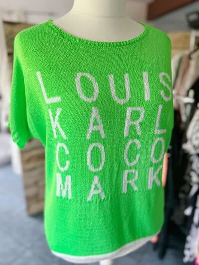 Der Sommerpulli von LKCM wird auf einer Schaufensterpuppe präsentiert, auf der die Namen „Louis“, „Karl“, „Coco“ und „Mark“ in weißer Schrift auf verschwommenem Kleiderständer-Hintergrund zu sehen sind.
