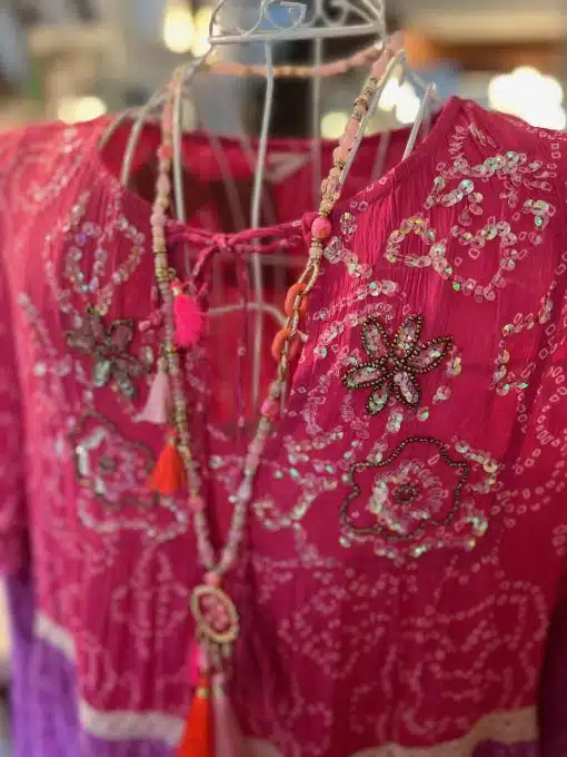 Eine Nahaufnahme eines leuchtend rosa Suntime Boho Kleid XL mit aufwendiger Perlen- und Paillettenstickerei, präsentiert auf einem Kleiderbügel, perfekt für Suntime.