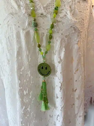 Eine Nahaufnahme einer Love Smile Kette (Kopie) mit einem Smiley-Anhänger und einer Quaste, präsentiert auf einer weißen Spitzenbluse.