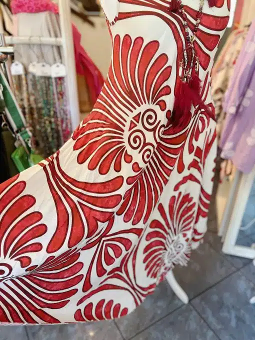 Eine Nahaufnahme eines Sommerkleids von Iland, das in einem Geschäft hängt und kräftige, wirbelnde und florale Muster aufweist. Im Hintergrund sind teilweise andere bunte Kleidungsstücke zu sehen.