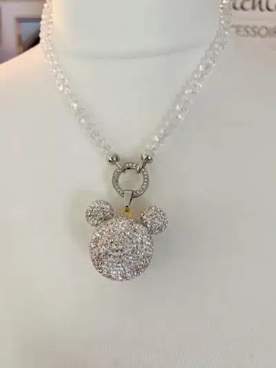 Eine Halskette mit einem funkelnden, kristallbesetzten Anhänger in Form eines Bärenkopfes. Der Maus-Wechselanhänger hat eine durchsichtige Perlenkette und wird auf einer weißen Schaufensterpuppenbüste präsentiert.