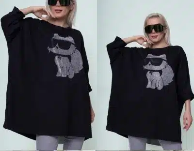 Eine Person, die das übergroße Cat Shirt trägt, auf dem eine Katze mit Sonnenbrille abgebildet ist, trägt auch eine große schwarze Sonnenbrille und graue Hosen. Das Outfit wird in zwei nebeneinanderliegenden Bildern aus leicht unterschiedlichen Winkeln gezeigt, was den unverwechselbaren Stil des Cat Shirts hervorhebt.