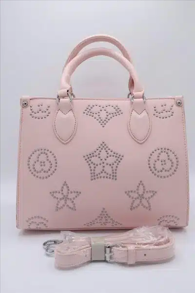 Eine rosa Handtasche ist mit silbernen Nieten verziert, die ein Stern- und Kreismuster bilden. Die Tasche hat zwei Griffe und einen passenden verstellbaren Riemen, der in Plastik eingewickelt und davor angebracht ist. Der Hintergrund ist schlicht weiß.