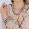 Eine Person ist mit einem auffälligen Magic Beads Metallic-Armband und einem dazu passenden Armband geschmückt, das ihre hellbeige, plissierte Bluse ergänzt. Das Bild zeigt den Oberkörper und einen Teil des Arms und deutet auf die Eleganz des Armbands hin, das diskret unter dem Stoff schimmert.
