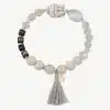 Das Buddha Love Armband ist ein Perlenarmband mit verschiedenen Perlen, darunter eine weiße Totenkopfperle, eine durchsichtige Perle und schwarze Perlen, die L,O,V,E ergeben. Es verfügt außerdem über ein kleines goldenes Etikett und ist mit einem grauen Quastenanhänger verziert.