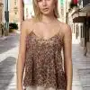 Eine Frau mit blondem Haar strahlt Glamour in dem Glamour Leopard Sequin Top aus, während sie auf einer sonnenbeschienenen Stadtstraße steht. Die Szene wird von Gebäuden im alten Stil unter einem klaren Himmel eingerahmt und schafft eine perfekte Mischung aus urbaner Eleganz und strahlendem Stil.