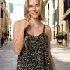 Eine Frau in einem glamourösen Leoparden-Paillettentop steht auf einer schmalen, gepflasterten Straße, die von Gebäuden gesäumt ist. Ihr blondes Haar fängt das Sonnenlicht ein, während sie in die Kamera lächelt. Es ist Tag und im Hintergrund ist ein Wolkenkratzer zu sehen, der ihren urbanen Glamour-Look unterstreicht.