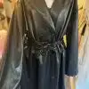Der schwarze Fashion Trenchcoat wird elegant auf einem Kleiderbügel präsentiert und hebt sein zweireihiges Design, das breite Revers und den gebundenen Taillengürtel hervor. Dieses Mode-Basic hebt sich vor einem sanft verschwommenen Hintergrund anderer Kleidungsstücke ab.