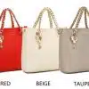 Fünf Handtaschen in Schwarz, Rot, Beige, Taupe und Weiß werden nebeneinander ausgestellt. Jede Tasche hat einen Kettenriemen und am Griff hängt ein dekorativer Anhänger. Die Farbe jeder Tasche ist darunter angegeben.
