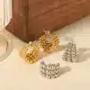 Ein Set aus vier Ohrringen wird auf einer hellen Stoffoberfläche präsentiert. Zwei sind aus Gold und weisen mehrere kleine Perlen in einem Schleifendesign auf. Die anderen beiden sind aus Silber und weisen eine ähnliche Perlenanordnung auf, einer in dreieckiger Form und der andere in gewellter Form.