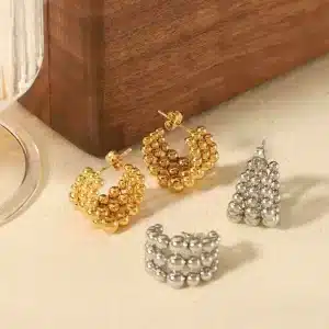 Ein Set aus vier Ohrringen wird auf einer hellen Stoffoberfläche präsentiert. Zwei sind aus Gold und weisen mehrere kleine Perlen in einem Schleifendesign auf. Die anderen beiden sind aus Silber und weisen eine ähnliche Perlenanordnung auf, einer in dreieckiger Form und der andere in gewellter Form