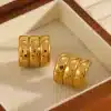 Ein Paar glänzende, goldene Daily-Ohrklemmen mit dreifachem Banddesign ruhen auf beigem Stoff in einer Holzbox.