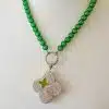 Entdecke deinen neuen Lieblingsschmuck: Eine Statement-Kette mit großen grünen Perlen und einem silbernen Anhänger in Form eines vierblättrigen Kleeblatts. Verziert mit funkelnden Steinchen und einem eleganten, zentralen Blütendesign bringt Sie jeden Look zum Strahlen. Präsentiert auf einer weißen Büste, offenbart sich dir der elegante Blüten-Wechselanhänger – dein perfektes Accessoire für vielseitigen Charme!.
