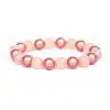 Das Armband „Magic Beads Pastell“ besteht aus pastellrosa-pfirsichfarbenen Perlen mit abwechselnd glänzenden und matten Oberflächen, die elegant in einem Kreis auf weißem Hintergrund angeordnet sind.