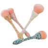 Vier Beauty Queen-Make-up-Pinsel mit glitzernden Griffen in Gold, Rosa, Weiß und Blaugrün mit rosa Borsten sind kreuz und quer auf einem schlichten weißen Hintergrund angeordnet. Diese Pinsel verleihen Ihrer Routine einen funkelnden Touch.