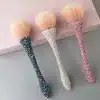 Drei Beauty Queen Make-up-Pinsel mit dicht gepackten, hellen Borsten und Griffen, die mit blauen, silbernen und rosa Strasssteinen besetzt sind, ruhen majestätisch auf einer grau-rosa Oberfläche. Ein wahrhaft königlicher Hauch für jeden Schönheitsliebhaber.