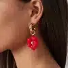 Entdecke deine stilvolle Seite! Stell dir vor: Du trägst ein atemberaubendes, rotes Blüten-Ohrring mit einem eleganten Goldbügel – einfach zum Verlieben. Im Zentrum der Blüte glänzt ein kleiner Edelstein und zieht alle Blicke auf sich. Dein Haar fällt glatt über deine Schultern und harmoniert perfekt mit deinem feurigen roten Top. Mach dich bereit, die Welt zu erobern – denn du bist ein Hingucker!.