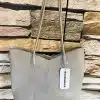 Stell dir vor: Eine angesagte beige Ledertasche mit doppelten Trägern, die lässig an einer stylischen Steinwand hängt. Die V-förmige Oberkante verleiht ihr einen zusätzlichen Hauch von Eleganz und das coole Tag am Träger setzt noch einen drauf. Ein Accessoire, das keine Wünsche offenlässt!.