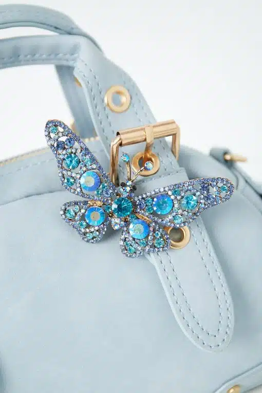 Lust auf ein echtes Statement-Piece? Die Butterfly Handbag in zartem Blau wartet auf dich! Goldene Hardware verleiht ihr einen edlen Twist, während die funkelnde Schmetterlings-Brosche mit blauen und türkisen Strassteinen direkt am Griff alle Blicke auf sich zieht. Das perfekte Accessoire, wenn du deinen Style aufs nächste Level heben willst – bist du bereit zu strahlen?.