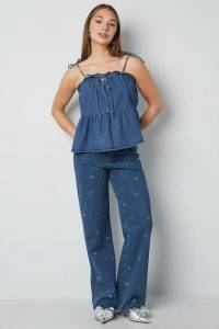 Klar! Hier ein moderner, werbewirksamer Text in der Du-Form, locker und direkt: Du bist bereit für den Sommer – das Denim-Top wartet schon auf dich! Mit verspielten Rüschen, coolen geknoteten Trägern und im angesagten Jeansblau bringt dieses Oberteil deinen Style aufs nächste Level. Kombiniere es wie ein echtes Fashion-Girl mit den passenden Wide-Leg-Jeans, die kleine gestickte Herzen als süßes Detail tragen. Für den letzten Schliff wählst du silberne Pointed-Toe-Schuhe und bist startklar: lässig, selbstbewusst und immer einen Schritt voraus. Zeig allen deinen modernen Denim-Look – stylisch war noch nie so einfach!